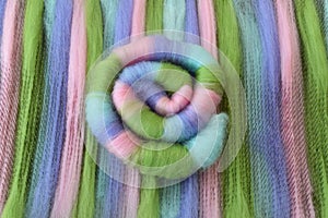 Green, pink, blue, and purple wool rolag coil on a blending board