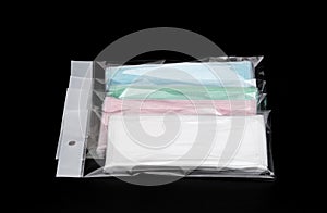 Green, pink, light blue and white ear loop disposable face mask in plastic bag overlapping, used for covering mouth and nose.