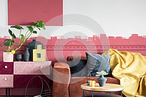 Green plant in white pot next to black and gold vases on pastel pink and burgundy shelf in living room with ombre wall and brown