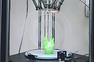 Green plastic 3D printed human hand stands in three-dimensional printer. Object model printed on automatic three dimensional 3d