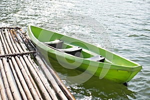 Green plastic boat parked at bamboo raft on water surface. this