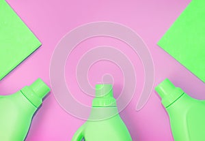 Green plastic bottles with chemicals for cleaning, rags for cleaning. Pink background