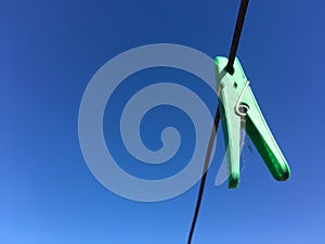 Green plastic clothespin clothes peg hanging from wire laundry line outdoors