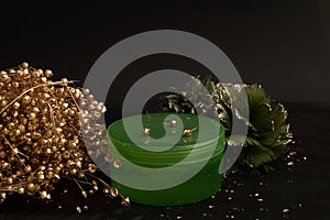 Green plastic container for balm cream cosmetics on black background with golden elements. Skin care concept, anti-aging