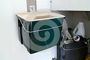 Green Plastic container for food waste/scraps. Trash cabinet inside a kitchen. Recycling/Composting