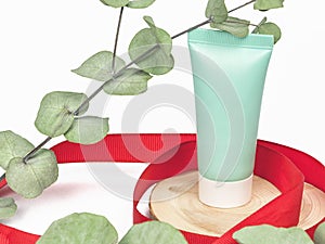 Green plastic cosmetic tube on a white background with leaves of eucalyptus
