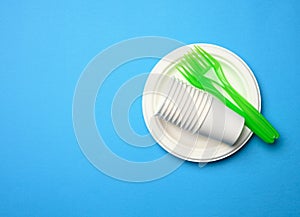 Green plastic forks and empty white paper disposable plates on a blue background