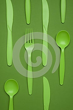 Green plastic forks, spoons, knifes on green paper. Set of plastic cutlery in different spoons forks knives and eco