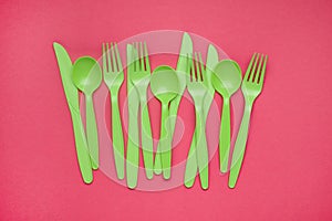 Green plastic forks, spoons, knifes on pink paper. Set of plastic cutlery in different spoons forks knives and eco