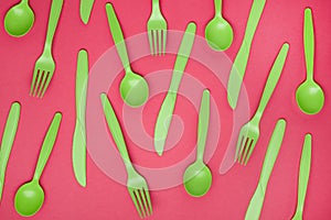 Green plastic forks, spoons, knifes on pink paper. Set of plastic cutlery in different spoons forks knives and eco