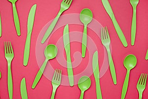 Green plastic forks, spoons, knifes on pink paper. Set of plastic cutlery in different spoons forks knives and eco-friendly