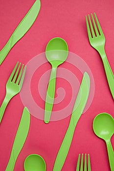 Green plastic forks, spoons, knifes on pink paper. Set of plastic cutlery in different spoons forks knives and eco-friendly