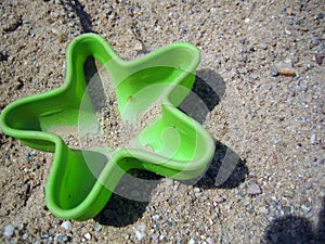 Green plastic sand toy shaped like a starfish lying in the sand