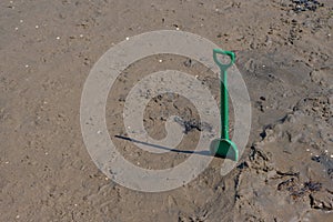 Green plastic shover standing in beach sand..