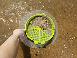 Green plastic tray or sieve in sand picking up shells and rocks