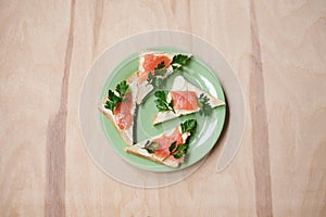 Green plate with salmon sandwiches with butter and parsley on wooden table. Buffet breakfast lunch meal. Healthy eating. Fish diet