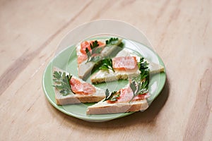 Green plate with salmon sandwiches with butter and parsley on wooden table. Buffet breakfast lunch meal. Healthy eating. Fish diet