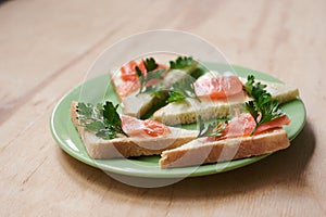 Green plate with salmon sandwiches with butter and parsley on wooden table. Buffet breakfast lunch meal. Healthy eating. Fish diet