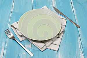 Green Plate with utensils and dish towel on blue wooden background with perspective