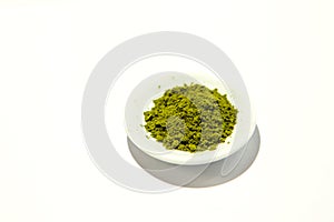 Green powder of Japanese matcha tea on a platter, isolated on a white background.