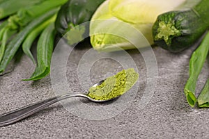 Green powder on spoon in front of raw green vegetables