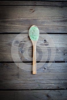 Green powder in spoon on old wooden table