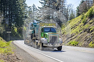 Green powerful big rig semi truck with oversize load yellow sign on the roof transporting crawler on the step down semi trailer