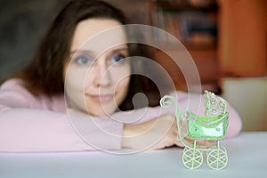 A green pram toy. The stroller in the foreground, a woman in the blur blurred. Desire to become a mother