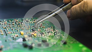 Green printed circuit board with all electric components being repaired by an caucasian engineer with the use of