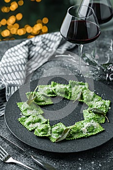 Green ravioli with spinach and ricotta cheese on plate over dark holiday background with glass of wine. Merry Christmas and New