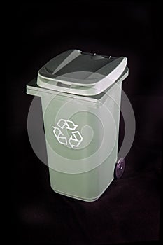 Green recycle rubbish or garbage bin with the recycle symbol on a black background