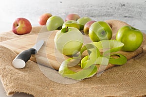 Green and red apples on a wooden cutting board. green apple peeled and kitchen knif close-up