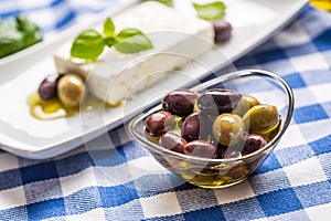 Green and red olives in bowl with olive oil and greek feta cheese in the background