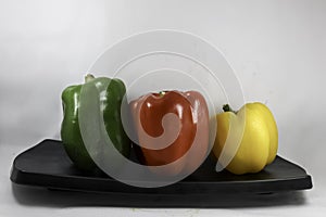 Green, red, yellow bell peppers on black platter