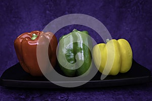 Green, red, yellow bell peppers on black platter. Dark background