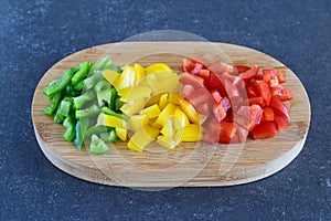 Green, red and yellow sweet paprika cut in cubes on a wooden cutting board on a dark abstract background. Step by step