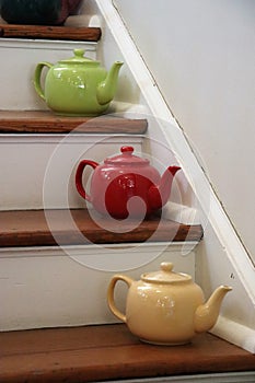 Green, red, and yellow teapots on wooden stairs