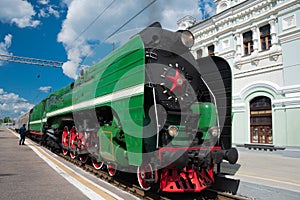 Green retro steam locomotive with red wheels arrived to the platform and building of Rizhsky Train Station