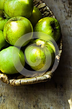 Green ripe organic bio apples, local produce, in rustic wicker basket on weathered wood table, harvest
