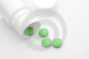Green round pharmaceutical pills spilling out of a white pill bottle. Medical conceptual photo, pharmacy theme.
