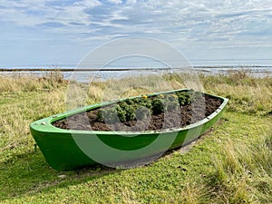 Green Rowing Boat Planter on grass with sea behind. Scottish Coast.