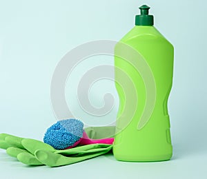 Green rubber gloves for cleanin and cleaning fluid in a plastic bottle on a blue background