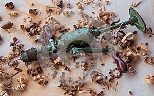 Green rusty metal ancient hand drill for carpentry on the workbench with wood chips around