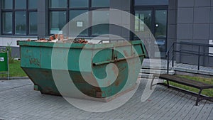 Green rusty metal container with brick debris at building