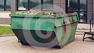 Green rusty metal container with orange brick debris against building