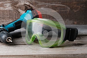 Green safety goggles and cordless drill on old vintage wooden background