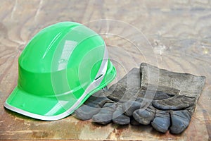 Green safety helmet and gauntlet cloves on a woode background