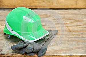 Green safety helmet and gauntlet cloves on a wooden background.