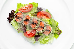 Green salad with salmon hot roll served with tomatoes on a white background. Salmon medallion appetizer.