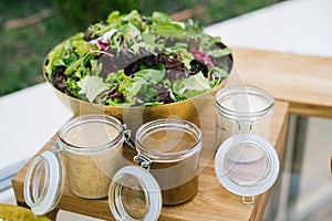 Green salad served in a bowl on a wooden table with three different dressings. photo